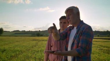 Yaşlı baba oğluyla yetiştirilmesi ve buğday sahada ayakta ve planı, güzel manzara arka planda söylüyorum tablet, holding planlama