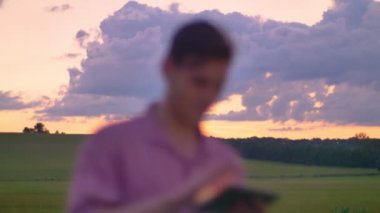 Tablete yazma ve buğday ya da çavdar sahada, güzel pembe gök yukarıda duran yakışıklı delikanlı.