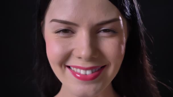 Очаровательная брюнетка с розовыми губами смотрит в камеру и улыбается, черный фон — стоковое видео