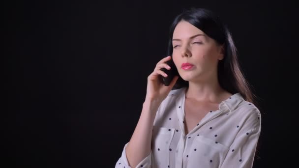 Nádherná zamyšlený mladý bruneta žena mluví o telefonu, stojící izolované na černém pozadí — Stock video