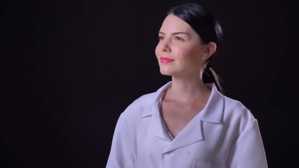 Affascinante giovane medico donna fiducioso in cappotto bianco sorridente alla macchina fotografica, in piedi isolato su sfondo nero — Video Stock