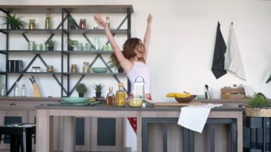 Kalp baskı ile komik pantolon giyen kameraya, gülümseyerek dans ve modern mutfak içinde atlama neşeli güzel kadın