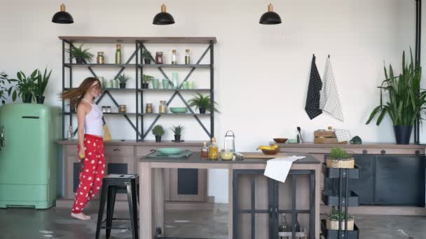 Mujer jengibre feliz en pijama sosteniendo espátula, bailando en la cocina y sonriente, alegre y alegre hembra en casa durante la mañana — Vídeo de stock