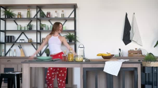 Mujer loca con pelo de jengibre bailando, cantando en espátula en la cocina y posando para la cámara, alegre y feliz — Vídeo de stock