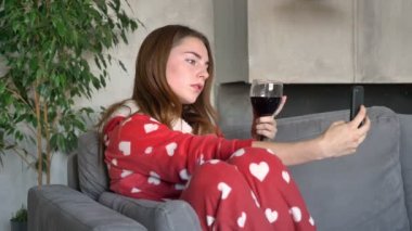 Selfie alma ve şarap, modern oturma odasında kanepede oturan tutan Kızıl saçlı güzel genç kadın