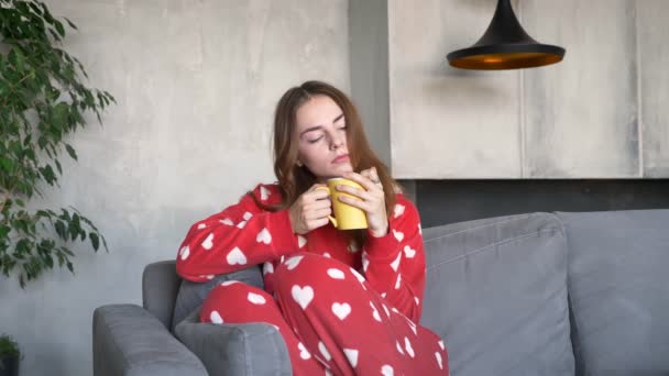Krásná mladá žena s nazrzlé vlasy pití kávy a sedí na pohovce v moderním obývacím pokoji, vážné a zamyšlený — Stock video