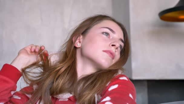 Happy ginger woman wearing red pajamas and looking at camera, smiling, sitting on couch in modern living room, daytime — Stock Video