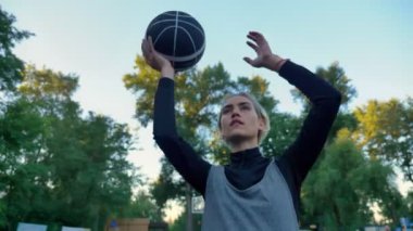 Yukarıda, düşük açılı mavi gökyüzü ile parkta oynarken topu atma güzel kadın basketbol oyuncusu