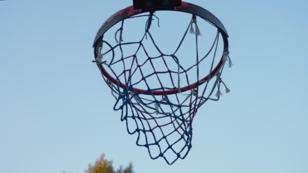 Throwing ball into basketball ring against blue sky, through hoop, outdoors — Stock Video