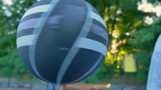 Mans hand balancing and spinning basketball on finger in open area, park in background — Stock Video