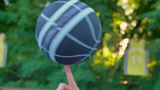 Basketball tournant et équilibrant sur un doigt avec des arbres en arrière-plan, au lever du soleil, jouant dans le parc — Video