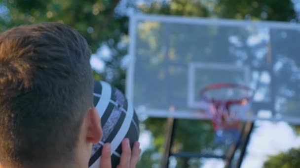 Schienale dell'uomo che lancia pallacanestro nel cerchio e cammina in avanti, palla che colpisce e attraversa il ring, gioca nel parco, all'aperto — Video Stock