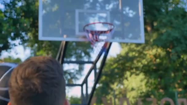 Baksidan av man hoppa och kasta basket, bollen träffar ringen, passerar genom hoop, spelar i parken, dagtid — Stockvideo