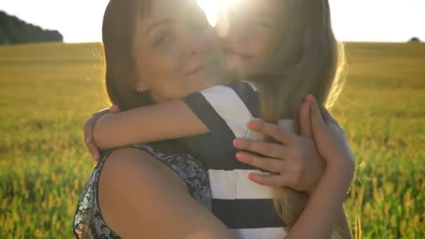 Menina feliz abraçando sua jovem mãe bonita e sorrindo, trigo ou campo de centeio durante o pôr do sol no fundo — Vídeo de Stock