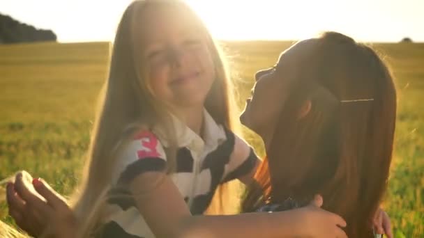 Pequena filha loira abraçando a jovem mãe e sorrindo, belo campo de trigo durante o pôr do sol no fundo — Vídeo de Stock