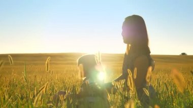 Sarılma ve gülümseyerek mutlu bir aile buğday alanında küçük kızı ile oturma ve günbatımı doğru işaret eden genç kadın