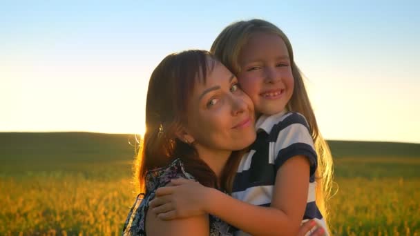 Retrato de madre joven y feliz abrazando a la pequeña hija rubia, mirando a la cámara y sonriendo, trigo o campo de centeno en el fondo — Vídeos de Stock