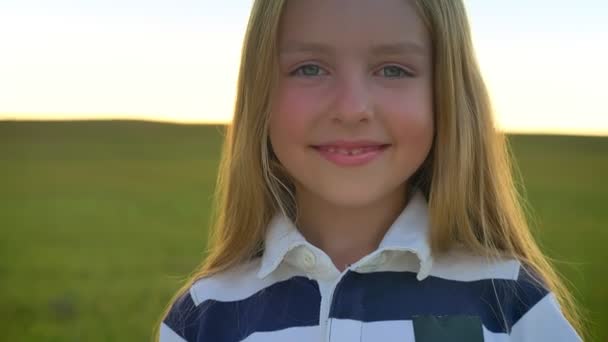 Bella bionda bambina sorridente alla macchina fotografica e girando la testa lontano, in piedi isolato sul campo di grano, bambino felice e allegro — Video Stock