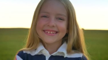 Gülüyor ve kamera, buğday alan arka plan, gün batımı sırasında gülümseyen mutlu sarışın küçük kız neşeli ve eğlenceli çocuk
