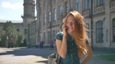 Mutlu genç kadın telefonda konuşurken zencefil ve gülümseyen, sokakta duran, arka planda Bina Saçında Rüzgar