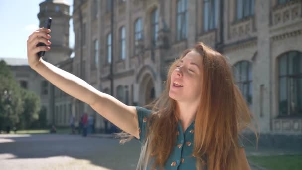 Αστεία τζίντζερ νεαρή γυναίκα να κάνει διαφορετικό πρόσωπο εκφράσεις και χαμογελώντας, λήψη selfie και στέκεται στον δρόμο — Αρχείο Βίντεο