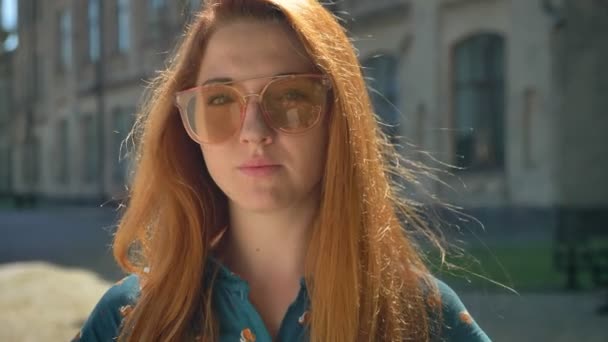 Serious trendy ginger woman looking at camera, standing on street, pensive and thoughtful emotions — Stock Video