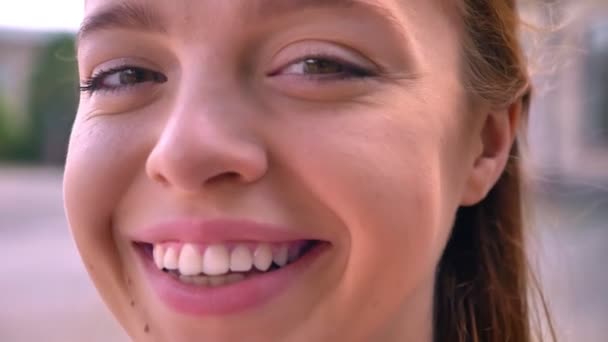 Zavřete záběry mladé zrzavé ženy se usmívá na fotoaparát, portrét šťastná a veselá žena, ulice v pozadí — Stock video