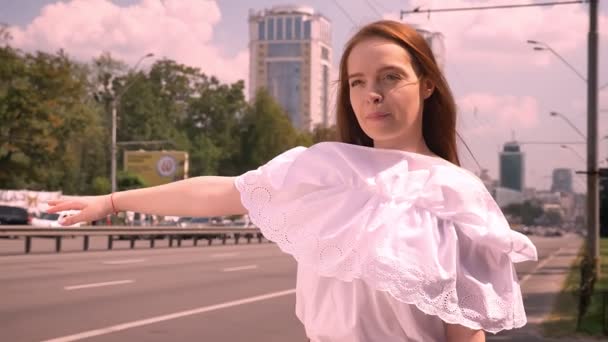 Belle jeune femme rousse sérieuse saluant taxi et debout sur la rue près de la route, charmante femme en chemise blanche — Video