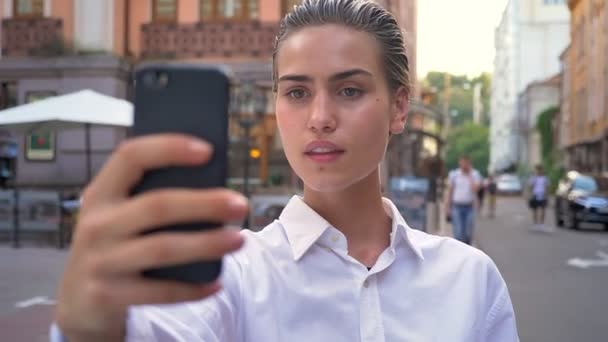 Giovane donna moderna è in piedi sulla strada e fare selfie su smartphone, sorridente, concetto di comunicazione, concetto urbano — Video Stock