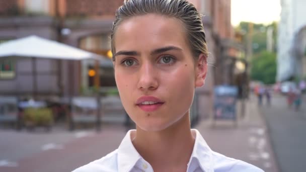 Thoughtful modern woman is walking in city and watching at camera in daytime, smiling, urban concept, blurred background — Stock Video
