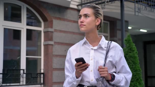 Mujer moderna joven está de pie en la calle y escribir mensaje en el teléfono inteligente, mirando a su alrededor, concepto de pensamiento, concepto de comunicación, concepto urbano — Vídeo de stock