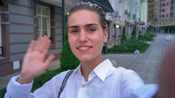 Mladá moderní žena stojící na ulici, drží fotoaparát, vlna hello, komunikační koncept — Stock video