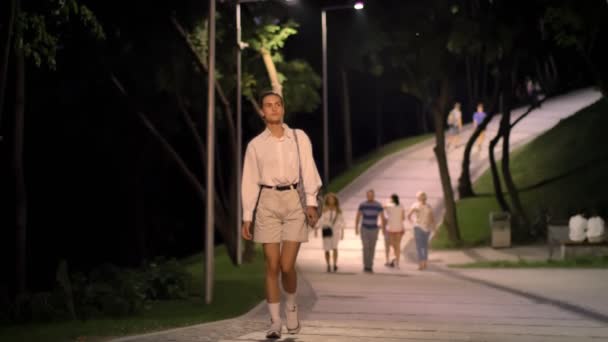 Jovem mulher moderna está andando rua abaixo no parque e assistindo ao redor à noite — Vídeo de Stock