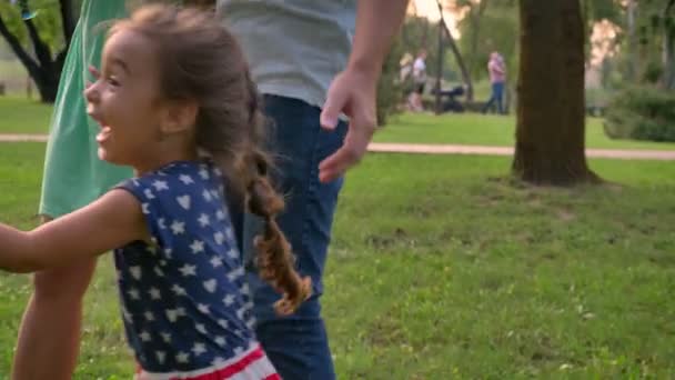 Молодая семья гуляет в парке летом, дочь бежит и ловит пузыри, концепция детства — стоковое видео