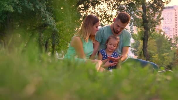 Ung familj sitter på matta i parken i sommar, dotter räknar, koppla av koncept — Stockvideo