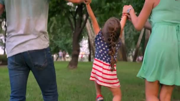 Joven familia está caminando en el parque en verano, sosteniendo y lanzando hija, jugando concepto — Vídeos de Stock