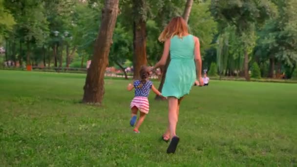 Jovem família está andando no parque no verão, os pais estão jogando pegar com a filha, jogando conceito — Vídeo de Stock