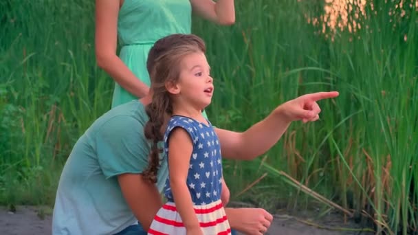 Knappe vader wijst op iets, zijn dochter luistert naar hem, familie concept, wandelen in het park op zonsondergang — Stockvideo