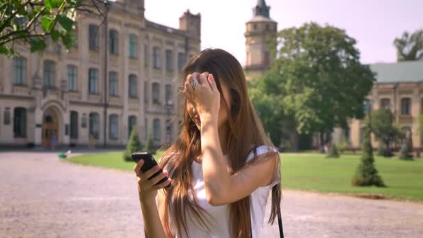 Sexy dama está de pie en el parque durante el día, leyendo el mensaje en el teléfono inteligente, concepto de comunicación — Vídeo de stock