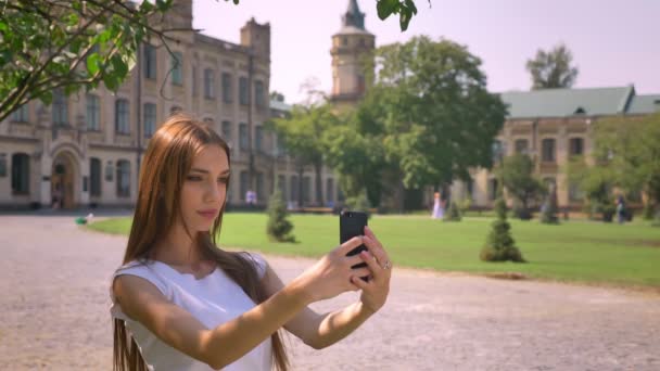 Sexy girl makes selfie on smartphone in park in daytime in summer, communication concept — Stock Video