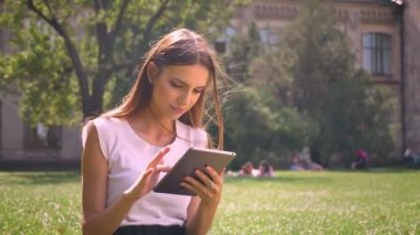 Seksi Bayan gündüz vakti parkta çimlerin üzerine oturuyor, tablete dokunarak, kavram, iletişim kavramı sakin ol