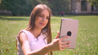 Seksi Bayan gündüz vakti parkta çimlerin üzerine oturuyor, tablete ara, kavram, iletişim kavramı relax video var