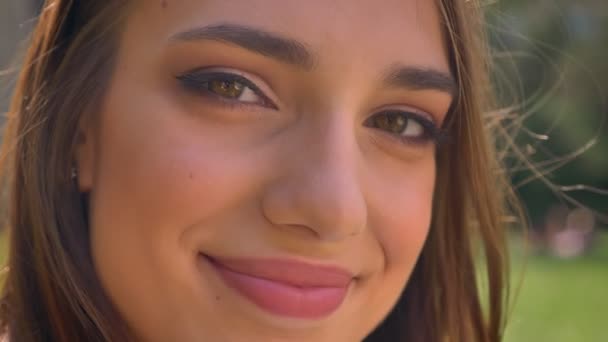 Csinos nő arcát figyeli a kamera parkban található nappali, szép mosoly, elmosódott háttér — Stock videók