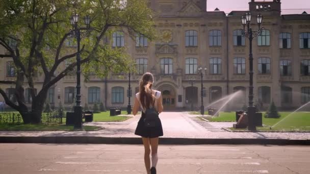 Силуэт молодой женщины переходит дорогу и прогулки вдоль до университета в парке в дневное время летом — стоковое видео
