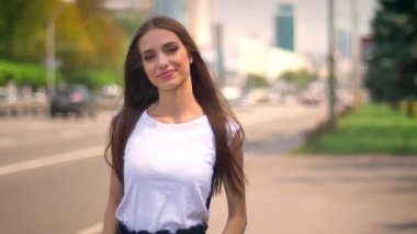 Seksi kadın üzerinde otobüs durağı gündüz yaz aylarında izlerken de kamera, gülümseyen, arka plan bulanık yolda duruyor