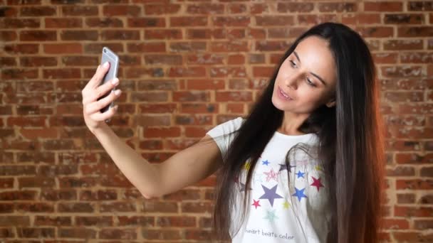 Schattig meisje doet selfie, smartphone, glimlachen, bakstenen muur op de achtergrond, portret — Stockvideo