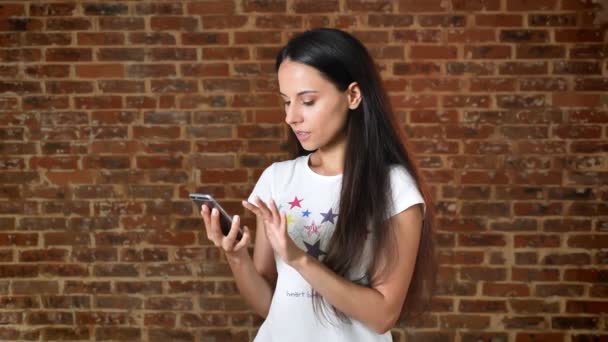 Young cute girl using smartphone, swiping, showing screen in camera, like sign, chroma key, brick wall in the background, portrait — Stock Video
