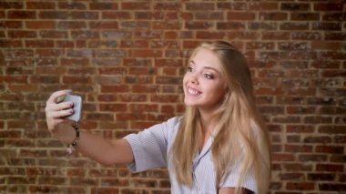 Selfie, gülen, gülümseyen, fotoğraf, smartphone, portre, tuğla duvar arka planda yapma genç beyaz sarışın.