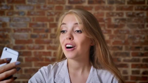 Jonge Kaukasische blonde praten op video chat, foto, smartphone, portret, bakstenen muur op de achtergrond — Stockvideo