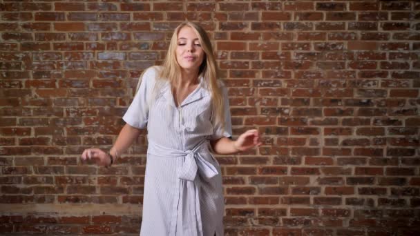Happy Young caucasian blonde smiling, dancing and looking at the camera, portrait, brick wall in the background — Stock Video